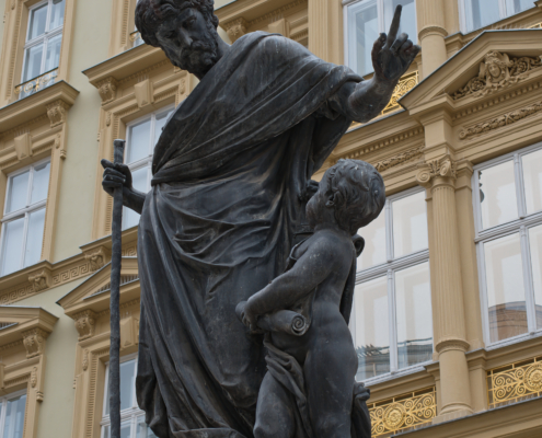 Statue mit Vater und Sohn am Graben mit gelben Haus im Hintergrund