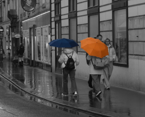 Schwarz-Weiß Bild mit 2 Personen. 1 Blauen und 1 Orangenen Regenschirm